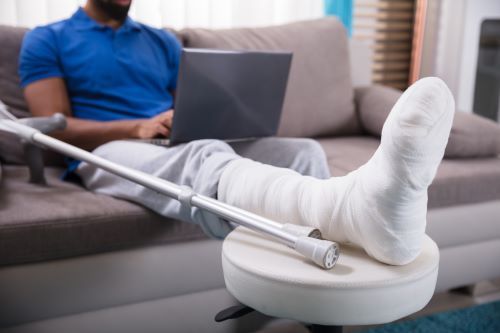 Man with personal injury to foot and crutches on laptop computer.