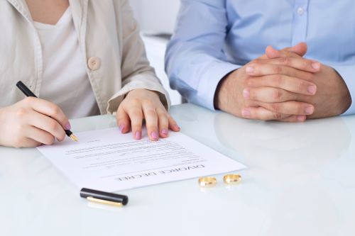 Man and woman signing Divorce Decree with gold wedding bands laying on table.